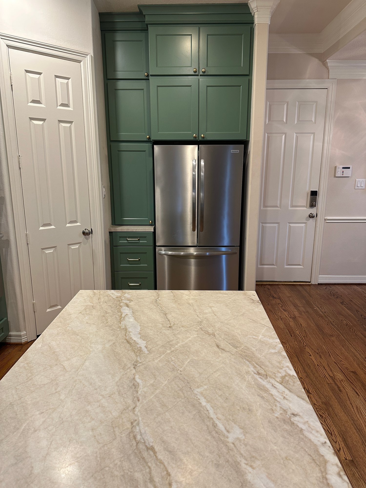 Kitchen renovation in a home in Houston, Texas, with built-in stainless steel French door refrigerator surrounded by sage green cabinetry, marble island counter in foreground.